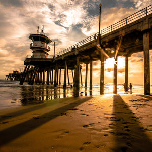 Low angle view of pier at beach against sky during sunset