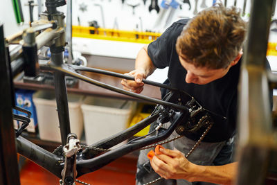 Focused male master wiping bike frame with rag while working in modern repair workshop