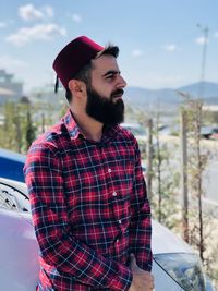 Man wearing hat looking away standing against sky