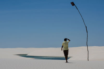 Rear view of man walking on sand at beach against clear sky