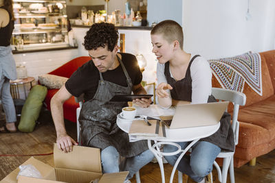 Male and female owners checking box while sitting on chair in cafe