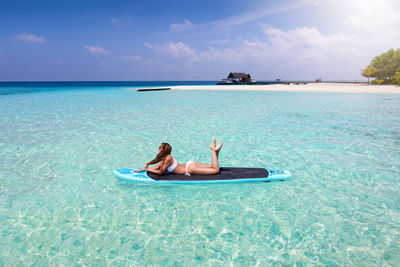 Woman on paddleboard in sea against sky