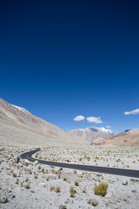 Scenic view of desert road against blue sky