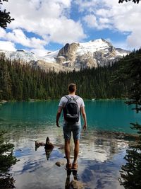 Rear view of man with dog walking on lake against sky