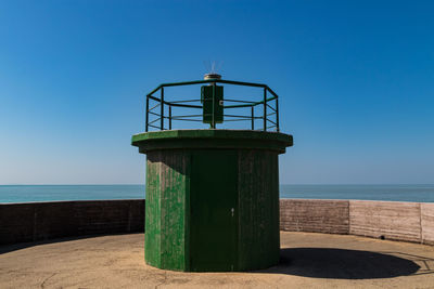 Lighthouse by sea against clear blue sky