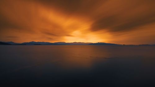 Scenic view of lake against dramatic sky during sunset