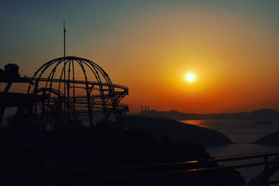 Silhouette ferris wheel against sea during sunset