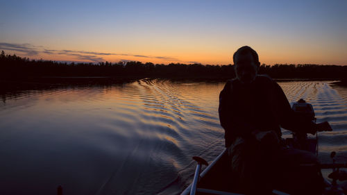 Silhouette man sitting on lake against sky during sunset