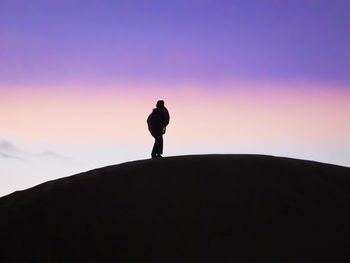 Silhouette man standing on rock against sky during sunset