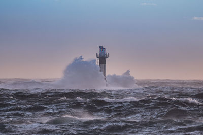 Lighthouse by sea against sky during sunset