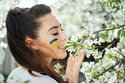 Outdoor portrait of ukrainian woman with blue and yellow ukrainian flag on her cheek on cherry