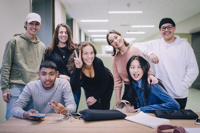 Portrait of teenage classmates making faces at desk in classroom