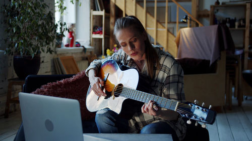 Woman learning guitar from laptop at home