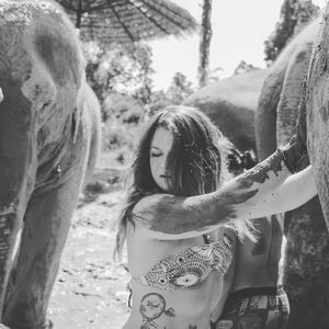 Young woman enjoying mud bath with elephant