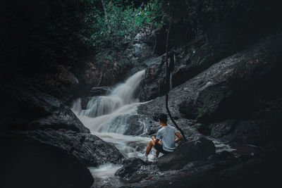 Man sitting on the rock looking at the waterfall background