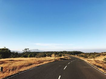 Road by agricultural field against clear blue sky