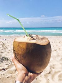 Close-up of hand holding coconut water at beach against sky