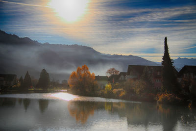 Scenic view of lake by buildings against sky during sunset