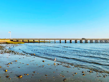 Pier over sea against clear blue sky