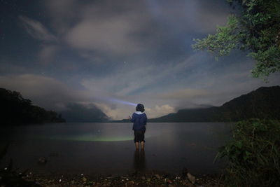 Rear view of man looking at lake against sky