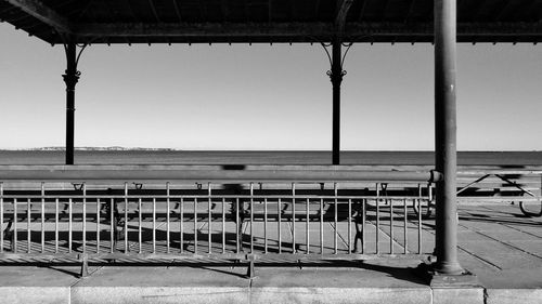 Empty seats on railing by sea against clear sky