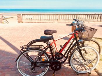 Bicycles on railing by sea against sky