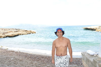 Portrait of shirtless man standing at beach against clear sky