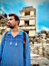 Man looking away while standing against building and blue sky