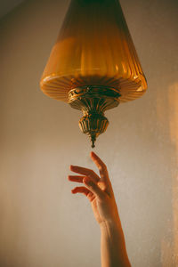 Close-up of hand holding electric lamp against wall