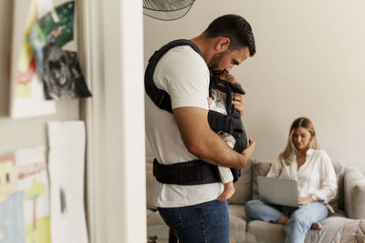 Side view of man kissing son while woman using laptop at home