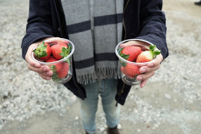 Low section of person holding disposable cups with strawberries