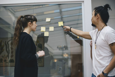 Male programmer explaining adhesive note to female colleague in office