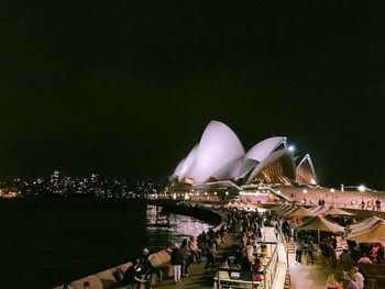 People in illuminated city against clear sky at night