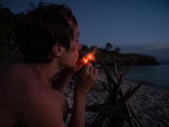 Man burning fire at beach against sky at dusk