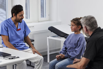 Male doctor talking to girl patient and grandfather during appointment
