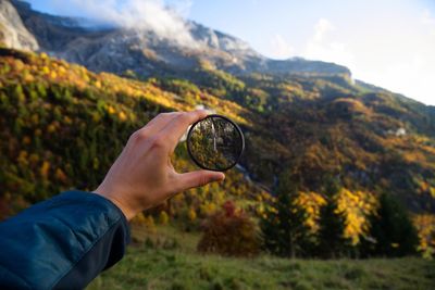 Close-up of hand holding lens against mountains