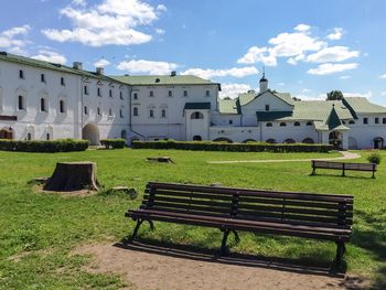 Empty bench on field by buildings against sky