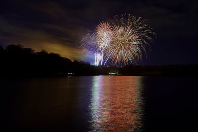 Firework display over lake against sky at night