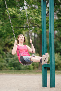 Full length of woman sitting on swing in playground