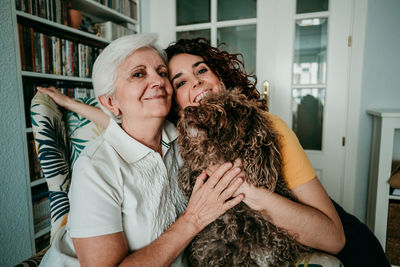 Portrait of smiling woman and daughter with dog sitting on armchair at home