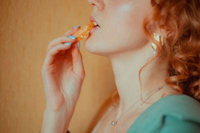 Midsection of young woman eating orange against wall at home