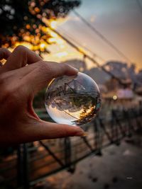 Cropped hand holding crystal ball with bridge reflecting during sunset