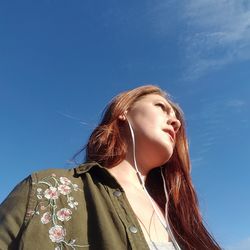 Low angle view of woman listening music from headphones against blue sky