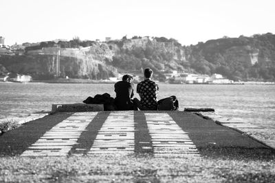 Men sitting on mountain against clear sky