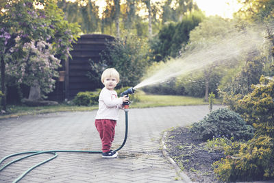 Side view of girl spraying water on plants with hose in park