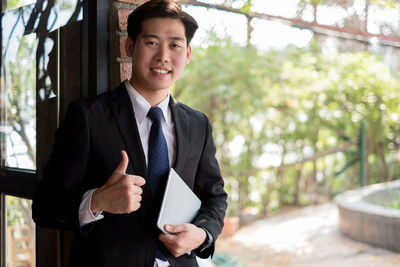 Portrait of smiling young businessman showing thumbs up while holding using digital tablet
