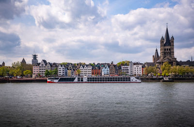 Buildings by river against cloudy sky