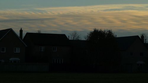 Silhouette houses on field against sky at sunset