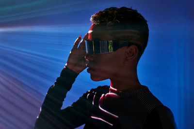 Side view of futuristic african american female in headset of virtual reality standing in dark studio with green beams of illumination while exploring cyberspace