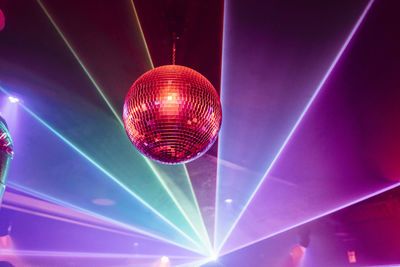 Modern disco ball shining under red neon light on ceiling of nightclub during party